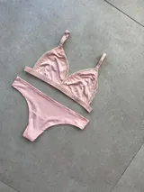 Conjunto de lencería compuesto por un corpiño triangular sin taza con detalles de encaje en los bordes y una bombacha tipo less de tiro medio, confeccionados en microfibra color rosa.