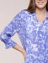 Blusa azul con estampado tipo pincelada en tonos blancos, cuello solapa con escote en V, media abotonadura frontal con botones nacarados, mangas tres cuartos con puños elásticos y diseño semi holgado.