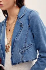 Saco corto de denim azul con solapas y bolsillos ribeteados, confeccionado en mezcla de algodón y poliéster.