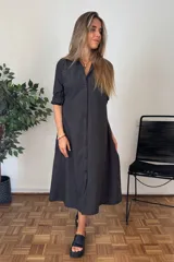 Vestido camisero largo color negro, de manga larga remangada, con cuello camisero y cierre frontal de botones. Corte amplio y falda con vuelo.