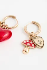 Aro tipo argolla dorada con dos dijes colgantes: un hongo rojo con blanco y un corazón dorado con una piedra brillante en el centro.