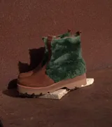 Botas de cuero marrón con la caña recubierta de corderito verde. Presentan una suela de plataforma tipo track en color beige y un tirador en la parte posterior para facilitar el calce.