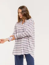 Camisa oversize a rayas horizontales azules y rojas sobre fondo blanco, con cuello mao, botones frontales, puños gruesos y frunces en la espalda.