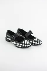 Zapato estilo Mary Jane confeccionado en cuero trenzado con diseño de damero en blanco y negro. Presenta una tira con hebilla circular en el empeine y un taco bajo cuadrado.