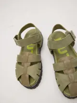 Sandalias de cuero marrón con tiras entrecruzadas, suela de goma negra con pespuntes blancos y hebilla lateral.