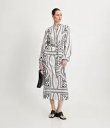 Vestido midi estilo chemise de satén con estampado de cadenas en blanco y negro. Tiene cuello redondo, mangas largas con puños elásticos, abotonadura frontal y cinturón con hebilla redonda.