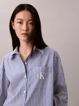 Camisa Calvin Klein de corte regular, con diseño de rayas verticales en tonos azul y blanco. Cuenta con cuello camisero, cierre frontal de botones, mangas largas y un bolsillo aplicado en el pecho con el logo bordado de la marca.