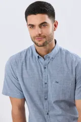 Camisa de manga corta confeccionada en mezcla de lino y algodón, con estampado de cuadros pequeños en tonos azules. Presenta cuello camisero con botones, cierre frontal abotonado, bolsillo aplicado en el pecho y dobladillo redondeado.