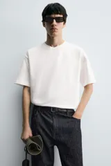 Camiseta blanca de corte holgado, cuello redondo y manga corta. Presenta un parche bordado en la espalda con diseño a contraste.