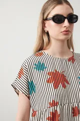 Vestido corto de silueta amplia con corte bajo busto, cuello a la base y mangas cortas. Presenta un estampado de lunares negros sobre fondo beige claro.