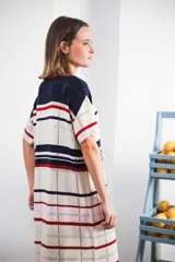 Vestido largo de tejido calado con rayas horizontales en tonos beige, marrón y amarillo. Tiene corte recto, hombros caídos, tajo lateral y logo bordado en la manga.