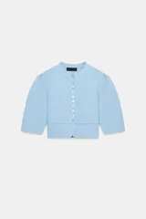 Chaqueta celeste de punto con cuello redondo, mangas cortas abullonadas y cierre frontal de botones.