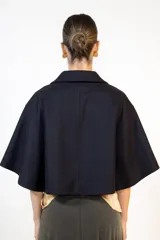 Capa de paño color negro con diseño de doble botonadura frontal y solapas clásicas. Presenta un corte holgado y mangas amplias tipo capa, confeccionada en tejido de poliéster.