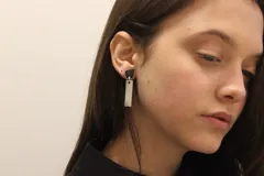 Aros colgantes con un pequeño rectángulo plateado colgando de una pieza geométrica negra.