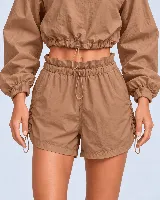 Short tipo clochard marrón de poliéster y poliamida, con cintura elástica ajustable mediante cordón, bolsillos laterales y fruncidos regulables en los laterales.