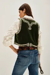 Chaleco corto de terciopelo en color verde oscuro, con bordados étnicos detallados en los bordes frontales y el ruedo. Presenta un diseño sin mangas y corte recto.