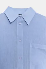 Camisa oversize color blanco, con cuello solapa, manga larga con puños marcados y cierre frontal de botones. Cuenta con un bolsillo de plastrón en el pecho y bajo asimétrico.