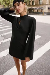 Vestido corto negro de cuello mao y escote en V, con mangas largas abanicadas y cierre de alamares en el frente. Cuenta con bolsillos frontales de plastrón y diseño de inspiración oriental.