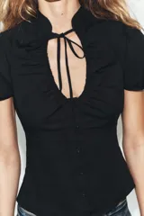 Top de popelín negro de manga corta abullonada, con cuello mao, escote en pico con lazada y cierre frontal con botones.