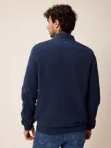 Cardigan de punto en color gris, con cierre frontal completo, cuello tipo mao y puños acanalados. Presenta un pequeño logo bordado en el pecho y detalles en contraste en el interior del cuello y puños.
