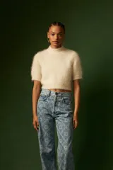 Top de punto de textura suave y esponjosa, color crudo, con cuello alto y mangas cortas. Presenta un corte cropped que llega a la cintura.