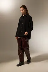 Sobrecamisa de jean color negro, con cierre frontal de botones metálicos, mangas largas y detalle de pequeñas tachas decorativas en la parte superior delantera.