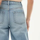 Jeans de mezclilla en tono azul medio con tiro alto y corte flare, con aberturas laterales en el dobladillo inferior.