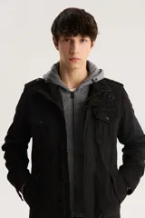 Campera militar negra con capucha gris de algodón, cierre frontal con cremallera y botones a presión, cuatro bolsillos frontales con solapa y charreteras en los hombros.