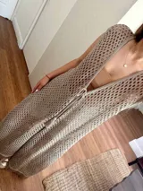 Chaleco largo de punto calado tipo red, color beige claro, con escote profundo en V, tiras para atar en el frente y flecos en el ruedo.