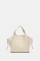 Bolso tipo city bandolera de color beige, con doble asa de mano, detalles de pespuntes y cremalleras laterales con tiradores. Cuenta con cierre imantado y compartimento interior extraíble.