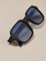 Gafas de sol de montura gruesa color negro, con forma cuadrada y lentes de cristal azul degradado.