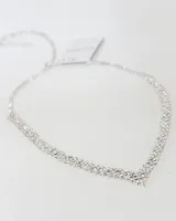 Collar de estilo gargantilla con diseño en forma de V, compuesto por múltiples hileras de cristales brillantes engarzados en metal plateado. Cuenta con cadena de extensión ajustable.
