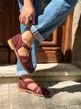 Sandalia tipo cangrejera de gamuza color bordó, con diseño cerrado de tiras cruzadas, talón cerrado y tira con hebilla metálica ajustable en el tobillo.