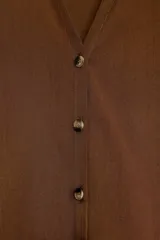 Camisa marrón de manga corta amplia, con cuello solapa y escote pico, cierre frontal con botones.