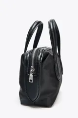 Bolso de mano tipo 'city' o 'bowling' pequeño, confeccionado en nylon negro. Posee asas dobles de material contrastante (posiblemente cuero o efecto charol) y una correa extraíble para llevar al hombro o cruzado.