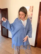 Saco tejido de punto color lavanda con diseño oversize, capucha integrada y detalle de flecos en el ruedo. Presenta mangas amplias y caída relajada.