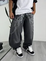 Pantalón de jean corte baggy, color gris oscuro con efecto lavado, estampado con diseño de cadenas en la parte superior frontal.