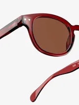 Lentes de sol redondos color rojo con lentes marrones y patillas negras.