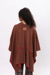 Ruana de algodón en color marrón con detalles de costura a mano en contraste color rojo en los bordes. Diseño envolvente de corte asimétrico y mangas amplias.