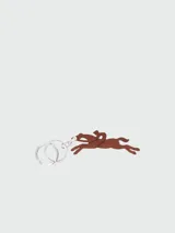Llavero Longchamp con dije de cuero marrón en forma de caballo con jinete y argollas metálicas plateadas grabadas con el nombre de la marca.