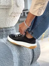 Zapatillas deportivas negras de cuero, con cordones y suela de goma blanca con base marrón.