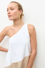 Maxi vestido largo de corte evasé, diseño bicolor con parte superior blanca y parte inferior beige, escote asimétrico de un solo hombro.