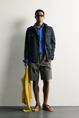 Chaqueta estilo militar relaxed fit de color azul marino, confeccionada en mezcla de algodón y lino. Presenta cuello subido, manga larga con puño abotonado, hombros con trabillas y cuatro bolsillos delanteros de parche con solapa. Se cierra al frente con botonadura metálica dorada.