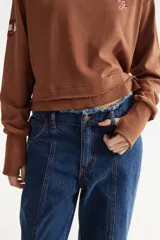 Buzo rústico marrón con cuello polera, mangas largas y calce boxy. Presenta costuras externas decorativas, puños acanalados y un bordado sutil en el pecho.