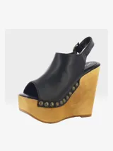 Sandalias de cuero negro con cuña alta de madera y plataforma delantera, detalle de tachas metálicas en los laterales y tira con hebilla en el talón.