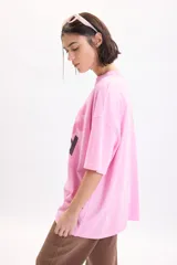 Remera oversize de manga corta en color rosado, con estampado gráfico frontal de una flor y la frase "Self Inspired" en tonos oscuros.