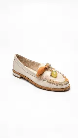 Mocasines de cuero color vainilla con taco bajo, punta redondeada y detalles artesanales de tiras entrelazadas en la parte superior. Incluyen un aplique decorativo con un dije colgante esférico translúcido.