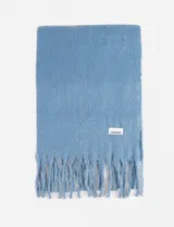 Bufanda de textura suave y abrigada en color celeste con destellos de lurex plateado. Presenta flecos en los extremos y una etiqueta de la marca Symphorine.