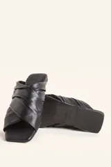 Sandalia tipo slide de cuero vacuno color blanco, con diseño de tiras cruzadas y fruncidas. Presenta una puntera cuadrada y una suela plana de cuero con un pequeño taco de 2 cm.