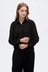 Camisa negra de poliéster con detalles de lurex y textura en relieve, corte holgado, mangas largas con puños y cierre frontal con botones.